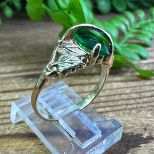 May include: A gold ring featuring a green gemstone set within a leaf design.