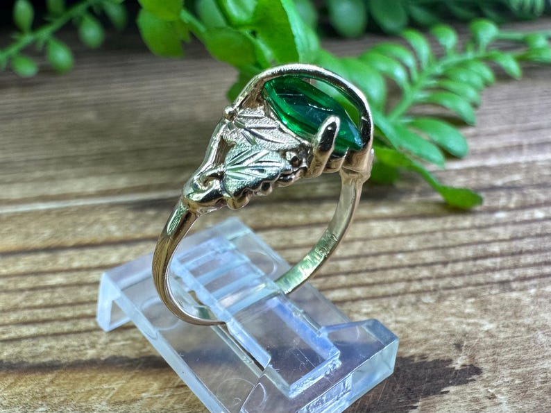 May include: A gold ring featuring a green gemstone set within a leaf design.