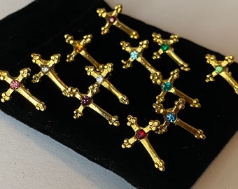 May include: Ten gold-tone cross charms with colourful rhinestones. The charms are arranged on a black velvet background.