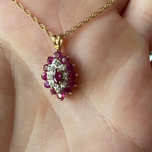 Op de afbeelding: Een gouden ketting met een marquisevormige hanger. De hanger is bezet met een centrale robijn in marquise-slijpvorm, omringd door een halo van kleine ronde diamanten, die weer is omringd door een cluster van ronde robijnen in gouden zettingen.