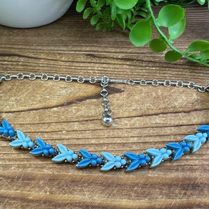 May include: A silver chain necklace with a blue and light blue glass leaf design. The necklace has a small silver ball charm.
