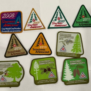 Peut inclure: Une collection de dix écussons brodés représentant les logos Scoutrees Arbrescout de 2008 à 2020. Chaque écusson représente une espèce d'arbre différente et l'année de sa création. Les écussons sont de forme rectangulaire et triangulaire et présentent une variété de couleurs, notamment le vert, le brun, le jaune et le rouge.