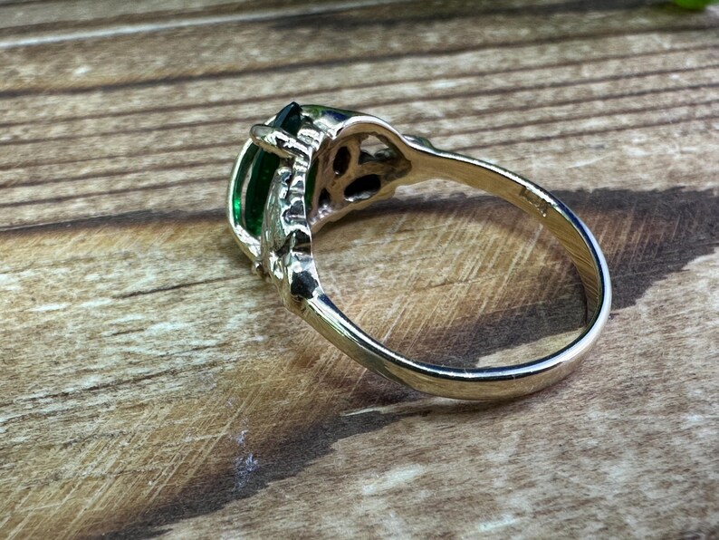May include: A silver ring with a large, emerald green gemstone set in a filigree design. The ring is on a wooden surface.