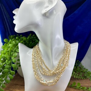 May include: A multi-strand necklace made of small, iridescent, gold-toned beads. The necklace is layered and has a delicate, feminine look.