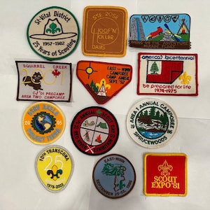 May include: A collection of ten embroidered patches featuring various scout camp themes. The patches are colourful and feature images of trees, tents, and other outdoor scenes. Some patches include text such as "Squirrel Creek", "East-Winn Camporee", and "Scout Expo '81".