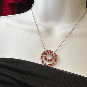 May include: A gold chain necklace with a double circle pendant set with red rubies.