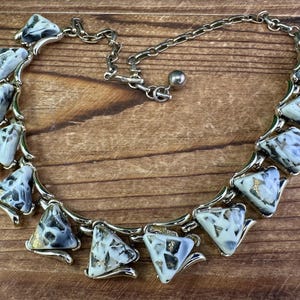 May include: A silver necklace with a chain and triangular-shaped pendants. The pendants are made of white and gray marble-like material with gold flecks.