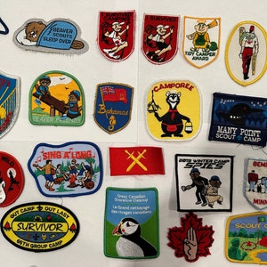 May include: A collection of colourful embroidered patches featuring various scout camp themes. The patches depict scenes of camping, nature, and scout activities. Some patches include text such as "Beaver Scouts Sleep Over", "Many Point Scout Camp", and "Survivor 66th Group Camp".