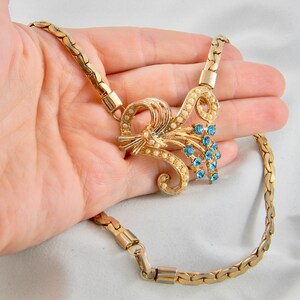May include: A gold chain necklace with a delicate floral design featuring faux pearls and blue rhinestones.