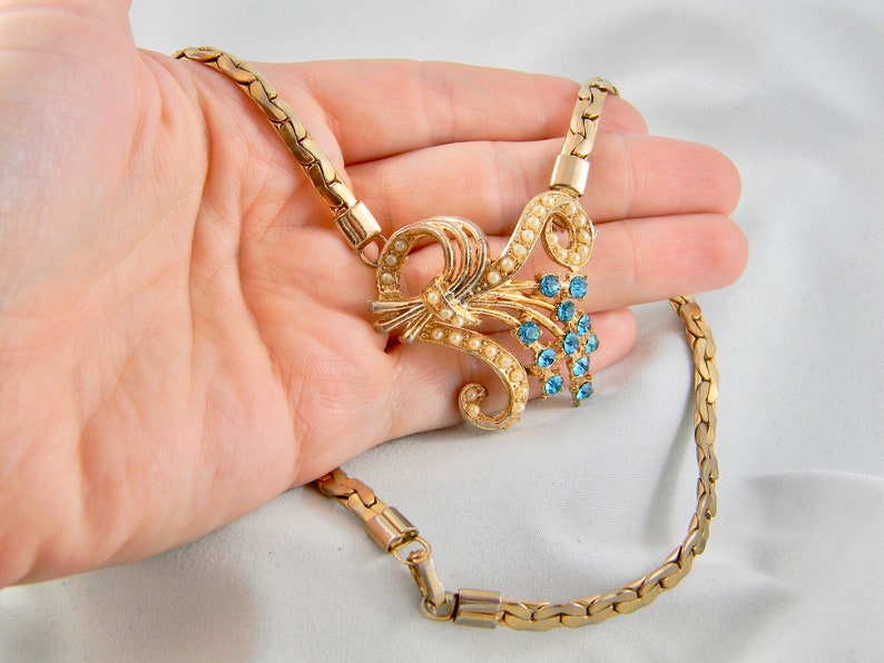 May include: A gold chain necklace with a delicate floral design featuring faux pearls and blue rhinestones.