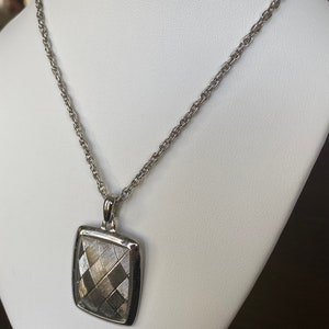May include: A silver chain necklace with a square pendant. The pendant has a textured, geometric design.