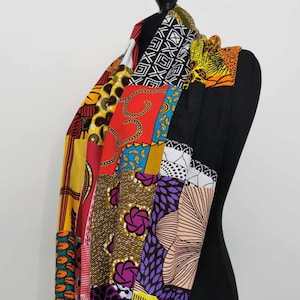 May include: A vibrant patchwork scarf displayed on a black mannequin. The scarf is made from a variety of colourful African wax print fabrics, including red, yellow, purple, and black, with geometric and floral designs.