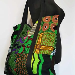May include: A patchwork tote bag with a black strap. The bag features a vibrant mix of green, orange, and black patterned fabrics. The bag is displayed on a black mannequin.