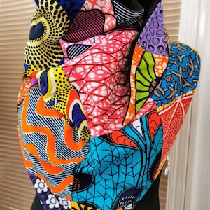 Könnte beinhalten: Ein bunter Patchwork-Schal aus verschiedenen afrikanischen Druckstoffen. Der Schal besteht aus verschiedenen geometrischen Mustern und leuchtenden Farben, darunter Rot, Gelb, Blau, Grün und Orange.