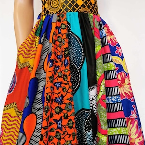 May include: A patchwork skirt in a variety of African wax print fabrics. The skirt features bold patterns in orange, blue, yellow, and black. It has a contrasting black waistband and a yellow and black patterned belt.