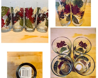 May include: Set of six clear glass tumblers with a fall leaf design. The glasses feature red, yellow, and green leaves with a white outline. The glasses are all the same size and shape. The glasses are on a wooden surface.