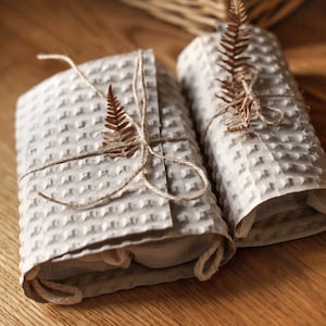 May include: Two gifts wrapped in brown paper with a waffle texture, tied with twine and decorated with dried fern leaves.