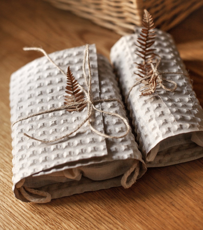 May include: Two gifts wrapped in brown paper with a waffle texture, tied with twine and decorated with dried fern leaves.