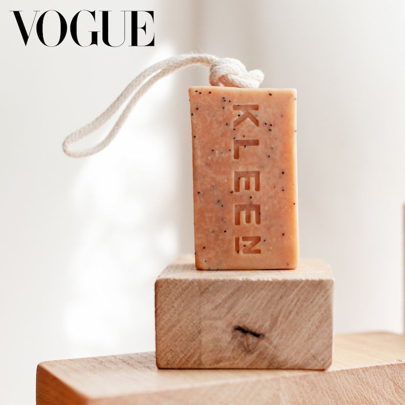 May include: A beige bar of soap with the word "KLEEN" embossed on it. The soap is tied with a white string and is sitting on a wooden block.