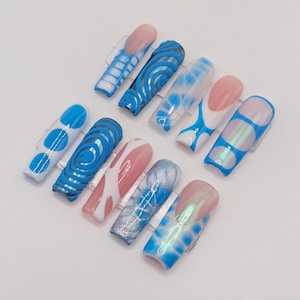 May include: A set of ten press-on nails in various designs. The nails feature a mix of blue, white, pink, and iridescent finishes. Designs include swirls, dots, and geometric patterns. The nails are displayed on a white surface.