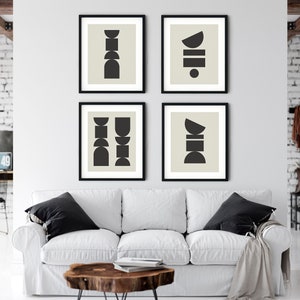 May include: Four black framed prints with abstract geometric shapes in black on a light beige background. The prints are arranged in a grid pattern on a white wall above a white couch.