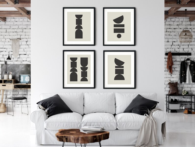 May include: Four black framed prints with abstract geometric shapes in black on a light beige background. The prints are arranged in a grid pattern on a white wall above a white couch.
