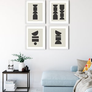 May include: Four framed prints with abstract geometric shapes in black on a beige background. The prints are arranged in a grid pattern on a white wall. The wall is in a living room setting with a light blue sofa, a side table, and a vase with greenery.