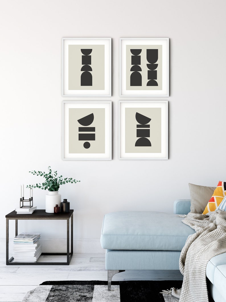May include: Four framed prints with abstract geometric shapes in black on a beige background. The prints are arranged in a grid pattern on a white wall. The wall is in a living room setting with a light blue sofa, a side table, and a vase with greenery.