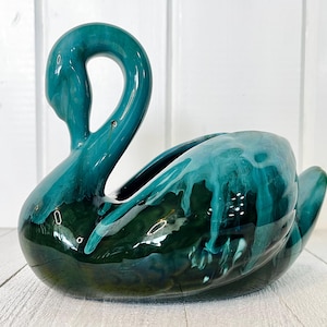 May include: A teal ceramic swan planter with a glossy finish. The swan has a long, curved neck and a wide, open body for planting. The planter is a decorative item, perfect for adding a touch of nature-inspired decor to any space.