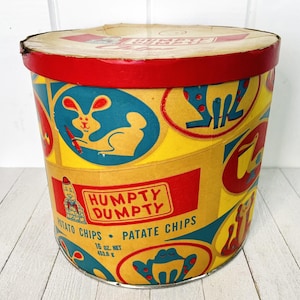 Puede incluir: Contenedor de patatas fritas Humpty Dumpty vintage. El contenedor cilíndrico presenta una tapa y base rojas, con un cuerpo amarillo adornado con ilustraciones de dibujos animados en rojo, azul y amarillo. El texto "Humpty Dumpty Potato Chips" es visible.