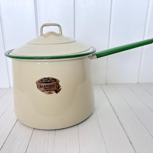 Puede incluir: Cacerola de esmalte color crema con tapa y asa verde. El borde y el asa también son verdes. La olla tiene una etiqueta que dice "AVENDISH WARE". La olla está sobre una superficie de madera blanca.