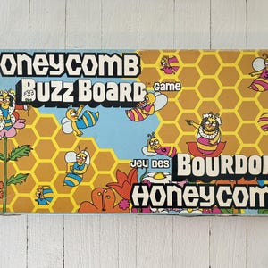 May include: Vintage Honeycomb Buzz Board game box. The box features a blue and yellow color scheme with cartoon bees and honeycomb patterns. Text includes "Honeycomb Buzz Board Game" and "Jeu des Bourdons Honeycomb".