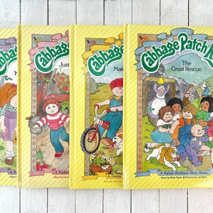 May include: Set of four yellow paperback books with illustrations of Cabbage Patch Kids characters. The books are titled "The Great Rescue", "Make a Wish", "Just Like Me", and "The Littlest Cabbage Patch Kid".