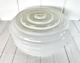 Puede incluir: Una lámpara de vidrio transparente y blanco con un diseño circular. La lámpara tiene una serie de anillos concéntricos y una forma redondeada. El vidrio es esmerilado y opaco, creando un brillo suave cuando se ilumina.
