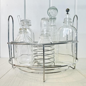 Peut inclure: Un ensemble de bar vintage avec des bouteilles en verre transparent et un support en métal. L'ensemble comprend des bouteilles de différentes formes et bouchons, et une paille en verre. Le support en métal a une poignée.