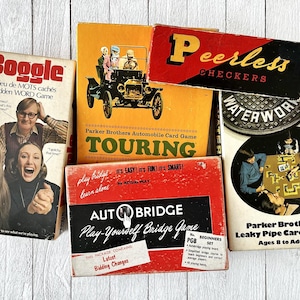 Peut inclure: Une collection de jeux de société vintage, dont Boggle, Touring, Peerless Checkers, Waterworks et Leaky Pipe. Les jeux sont tous dans leurs boîtes d'origine et présentent des illustrations colorées.