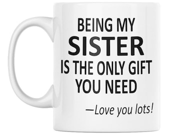 Puede incluir: Una taza de cerámica blanca con un asa en el lado izquierdo. La taza presenta un texto impreso en negro que dice: BEING MY SISTER IS THE ONLY GIFT YOU NEED —Love you lots! El diseño está centrado en la parte frontal de la superficie blanca.