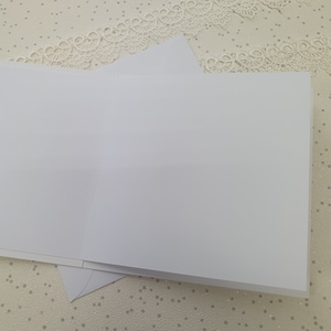 May include: Two blank white greeting cards stacked on top of each other. The cards are on a white background with a white lace pattern.