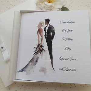 May include: A white card with a watercolor illustration of a bride and groom. The text reads "Congratulations on your Wedding Day Lottie and Jason 26th April 2024".
