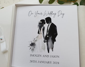 Może przedstawiać: Biała kartka ślubna z czarno-białym sylwetką pary całującej się. Na kartce widnieje napis "On Your Wedding Day" oraz imiona "IMOGEN AND JASON" i data "26TH JANUARY 2024".