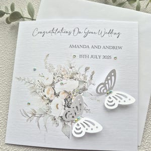 May include: A white wedding card with a floral design and two white butterflies. The card says "Congratulations on your wedding" and "Amanda and Andrew" with the date "15th July 2025".