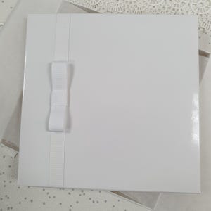 May include: A white card with a white satin ribbon and bow. The card is blank and ready for writing.