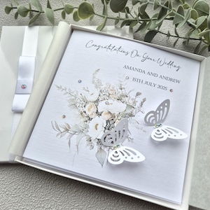 May include: White wedding card with a floral design and two white butterflies. The card reads "Congratulations On Your Wedding" and "Amanda and Andrew 15th July 2025".