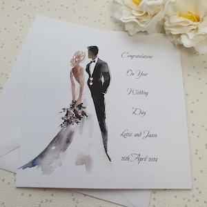 May include: A white wedding card with a watercolor illustration of a bride and groom. The text reads "Congratulations on your Wedding Day Lottie and Jason 26th April 2024".