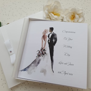 May include: A white wedding card with a watercolor illustration of a bride and groom. The card reads "Congratulations on your Wedding Day Lattie and Jason 26th April 2024".