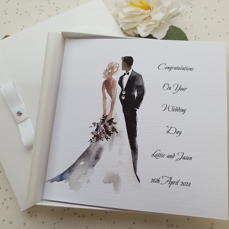 May include: A white card with a watercolor illustration of a bride and groom. The card says "Congratulations on your Wedding Day Lottie and Jason 26th April 2024".