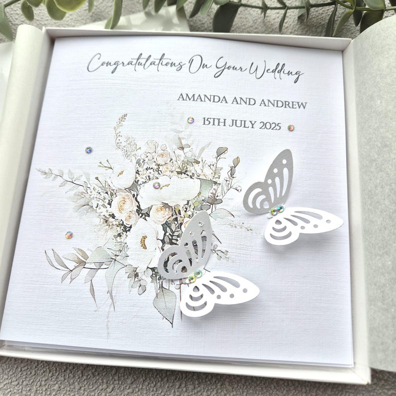 May include: A white card with a floral design and two white butterflies. The card says "Congratulations on your wedding" and "Amanda and Andrew 15th July 2025".