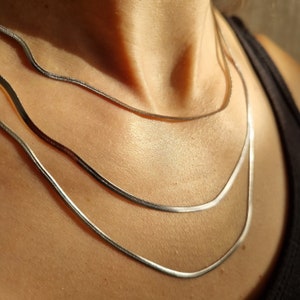 May include: Three silver chain necklaces layered on a person's neck. The chains are of different widths and lengths.