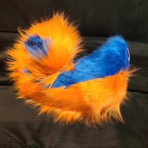 May include: A fluffy orange and blue tail with a long, flowing orange fur and a shorter, blue fur section. The tail is curled up and appears to be made of soft, plush material.