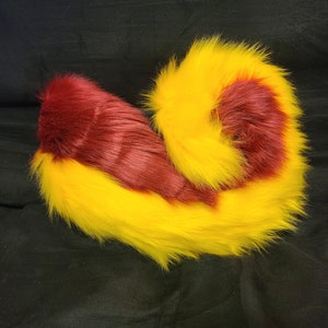 May include: A fluffy, two-toned tail with a yellow base and a burgundy tip. The tail is curled into a spiral shape.